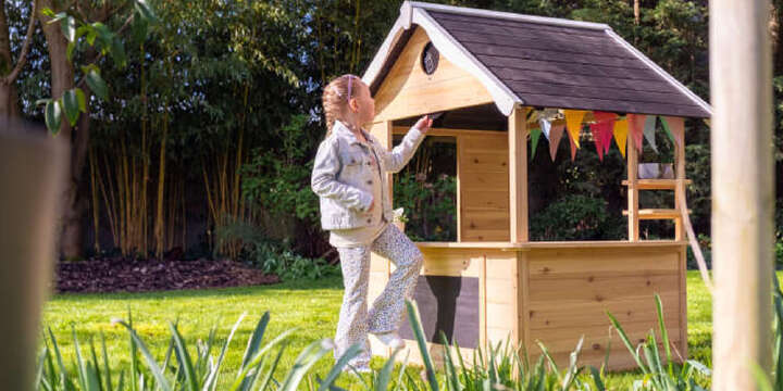 maedchen steht am holzspielhaus im garten 1000x500